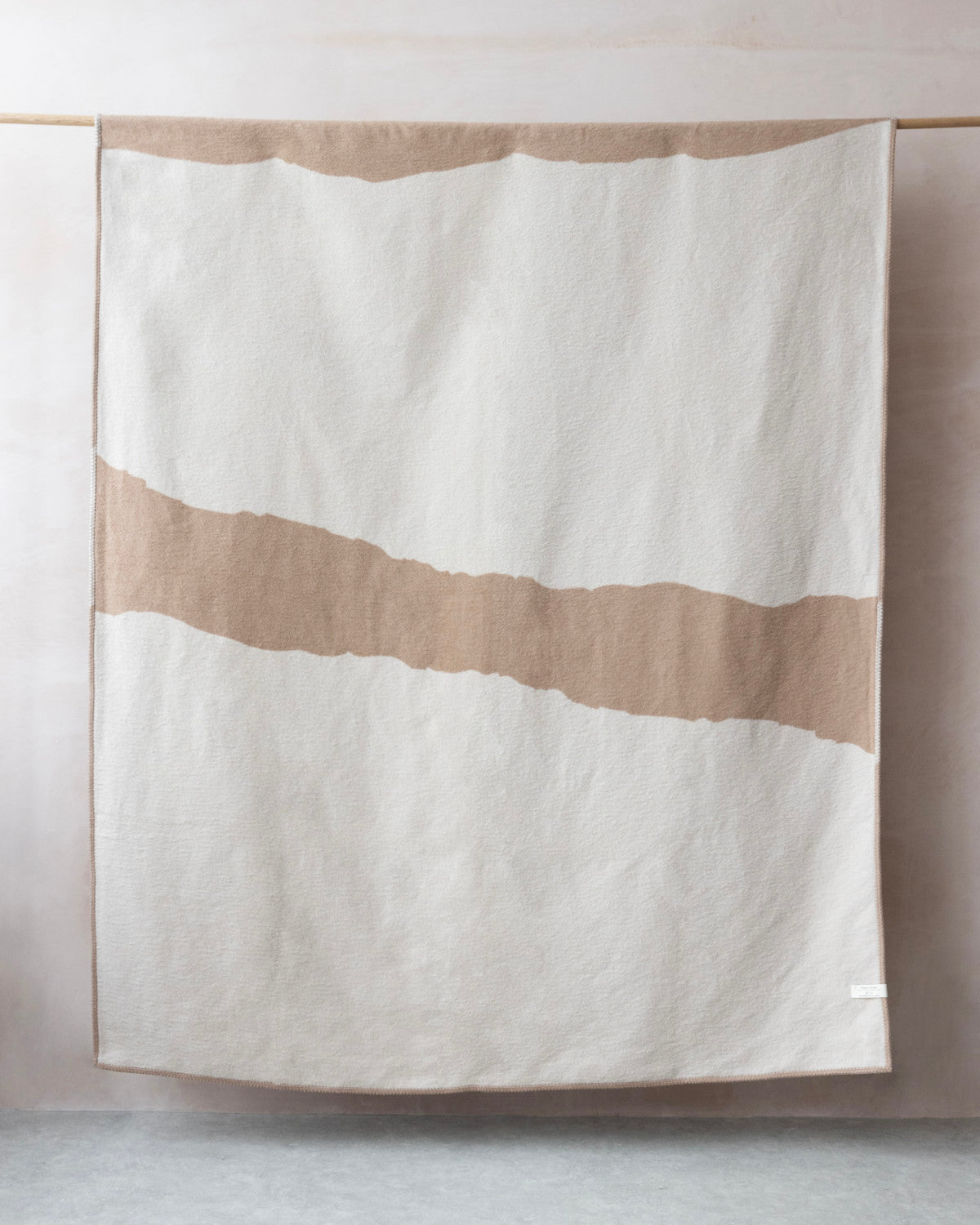 Cloud Cotton Blanket: Strata in Clay, showcasing a cream base with a tan stripe, draped over a rod, highlighting its soft, brushed texture and blanket-stitched edge.
