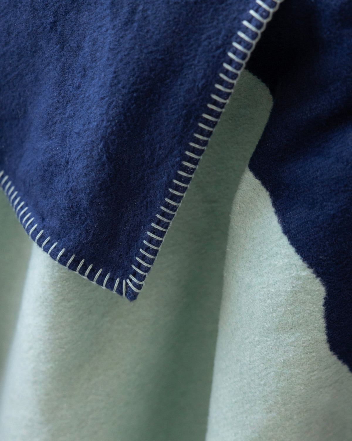 Cloud Cotton Blanket: Vale in Mistral showcases a navy-blue top and mint-green underside, joined by contrasting stitching, offering a soft, fleece-like texture.