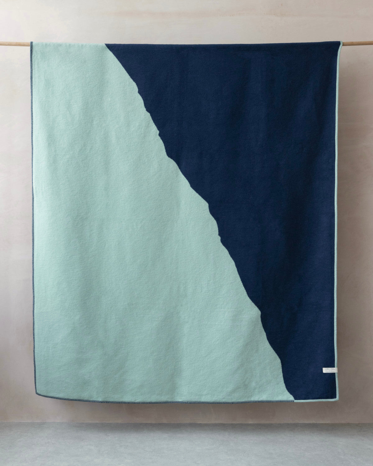 Cloud Cotton Blanket: Vale in Mistral, draped on a rod, features mint-green and navy panels with a label, showcasing a soft, brushed finish.