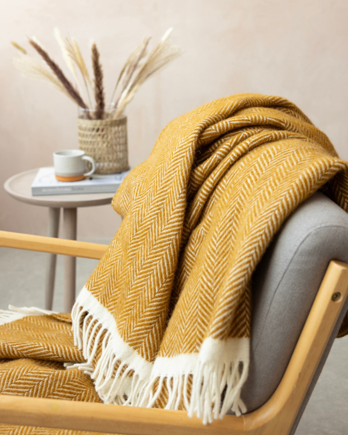 Clifton Blanket Gift Box: Spiced Cider featuring a mustard herringbone blanket draped on a wooden chair, with a cozy side table setup.