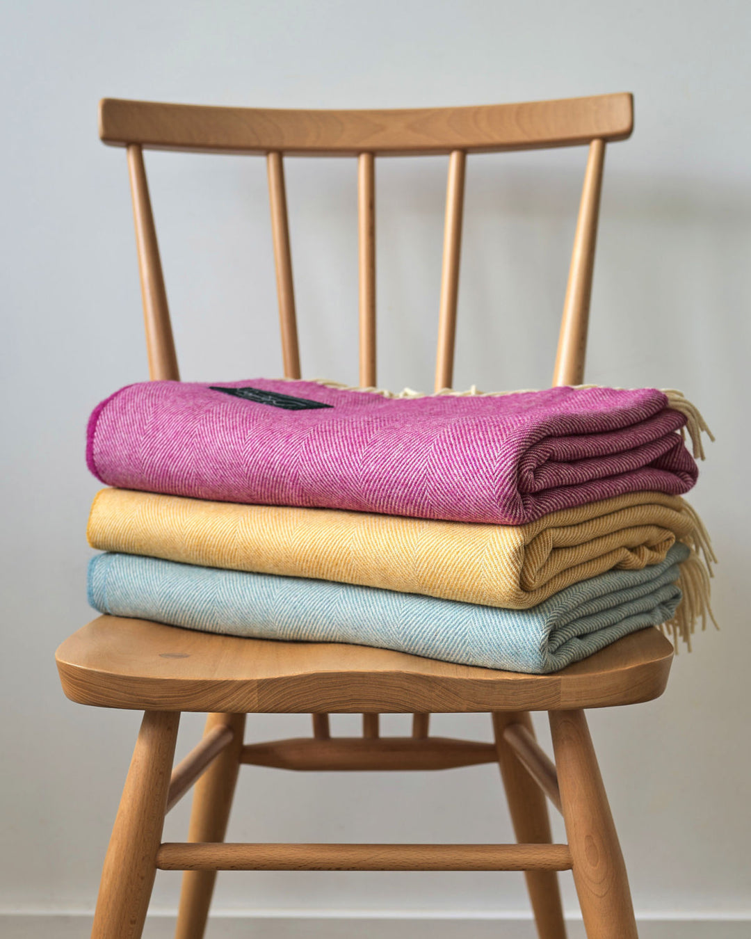 Stack of pink, yellow and blue merino wool throw on a chair from The British Blanket Company