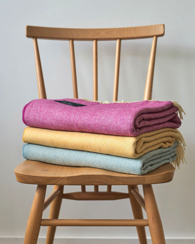 Stack of pink, yellow and blue merino wool throw on a chair from The British Blanket Company