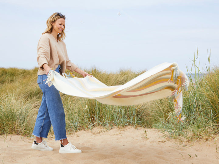 Woman on the beach laying blanket on the sand Pastel Rainbow Stripe Herringbone Throw by The British Blanket Company