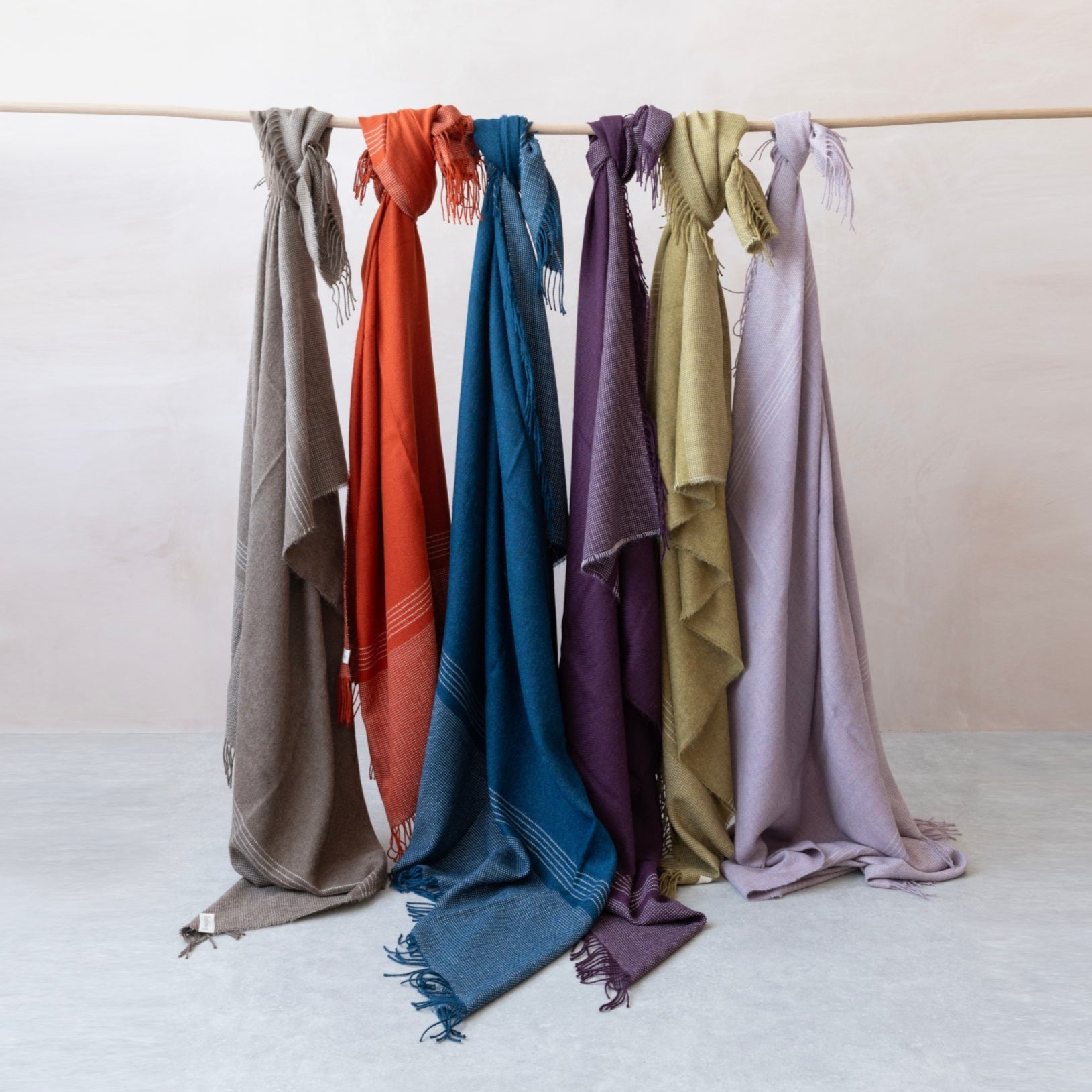 100% Alpaca Collection featuring 6 blankets in different shades tied to a pole, draping to the floor. 