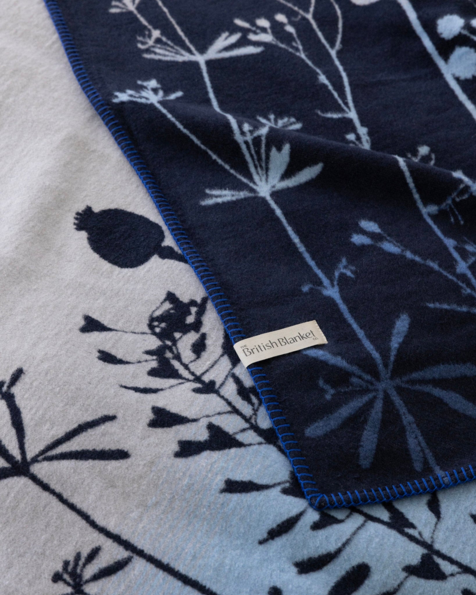 The SECOND Clarissa Hulse Blanket: Seedheads in Midnight features folded wool with silhouetted wildflower motifs and a whip-stitch edge, showcasing elegant craftsmanship.