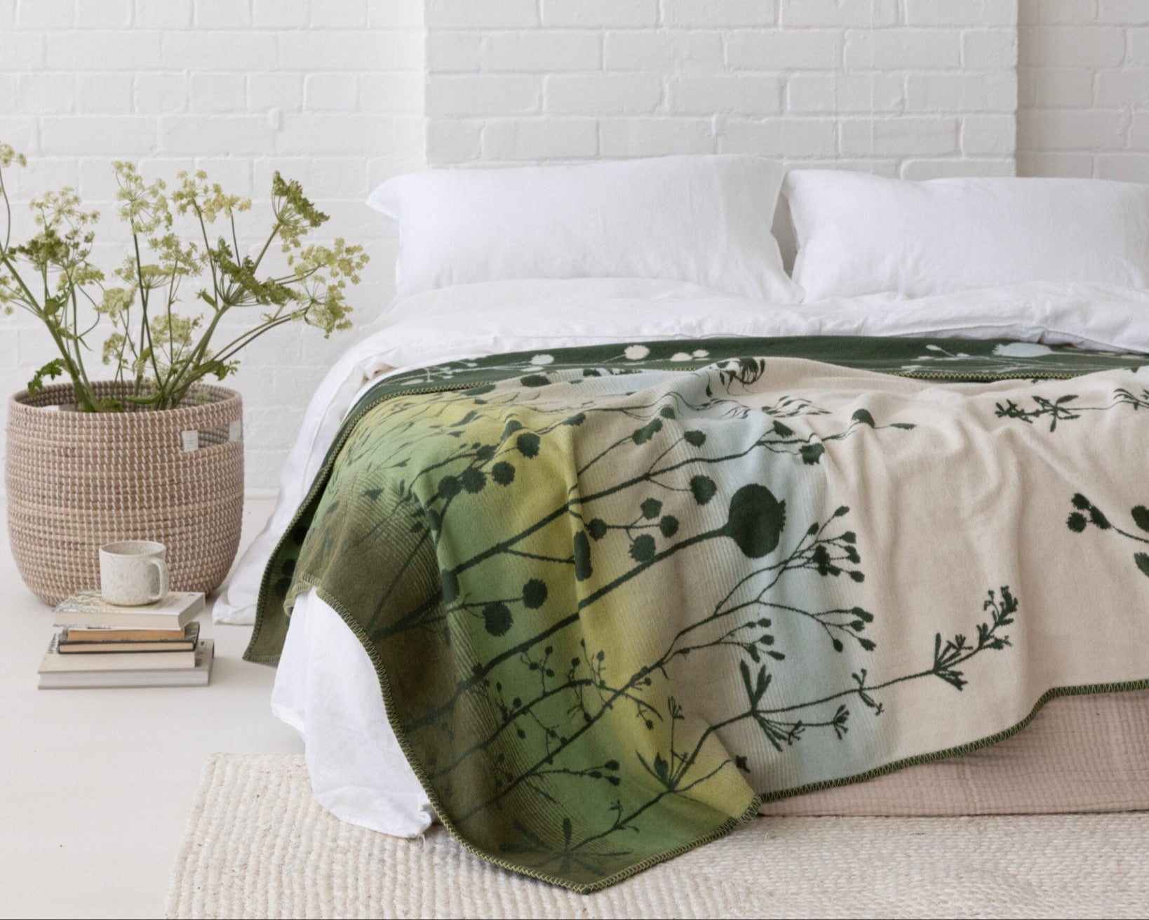 Clarissa Hulse Blanket: Seedheads in Moss on a bed, showcasing its green ombré pattern and wildflower-inspired design, complemented by a calm, natural bedroom setting.