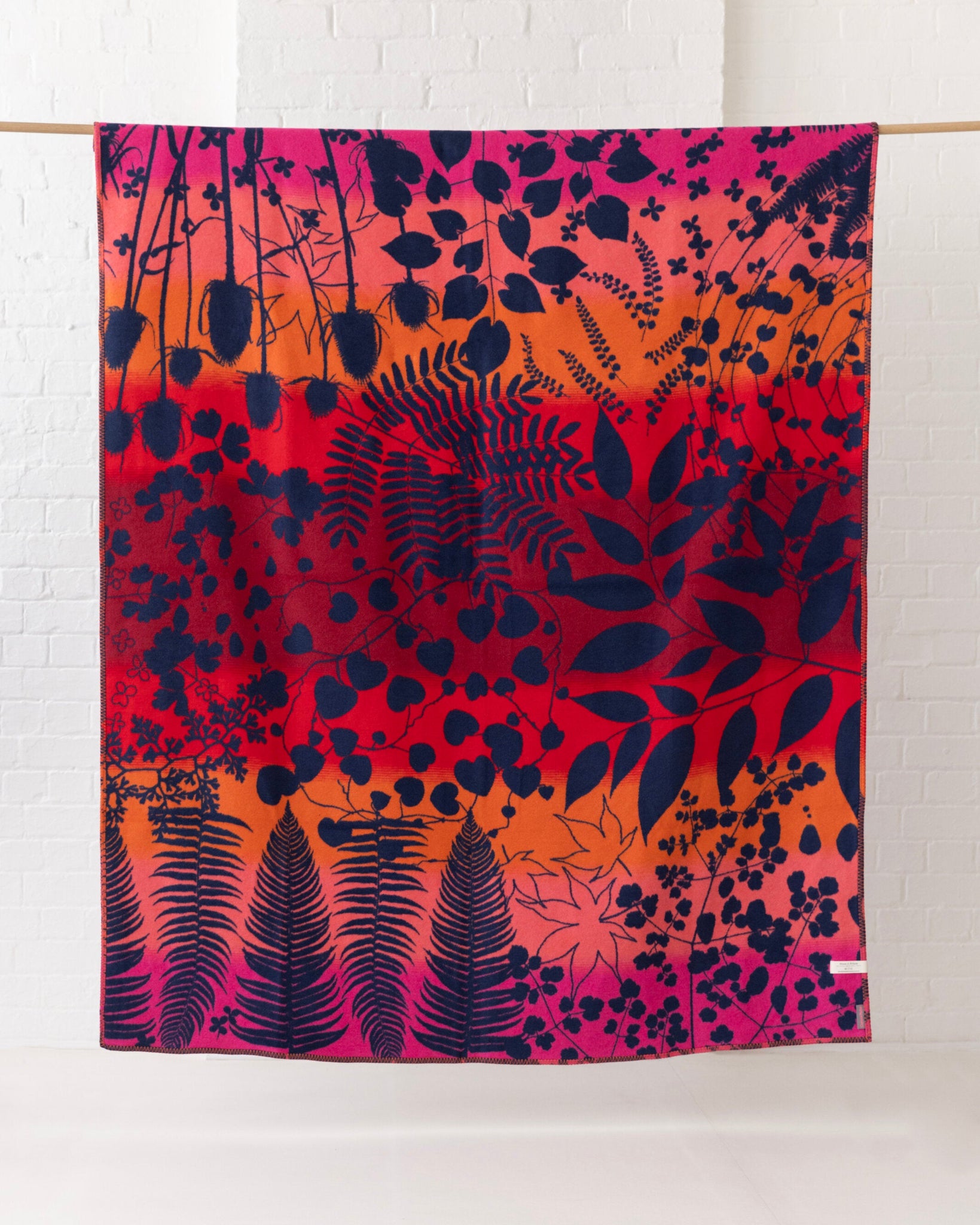 Clarissa Hulse Blanket: Indian Summer in Sunset, featuring a vibrant botanical ombré design with navy silhouettes on a woven cotton throw, showcased as decorative home décor.