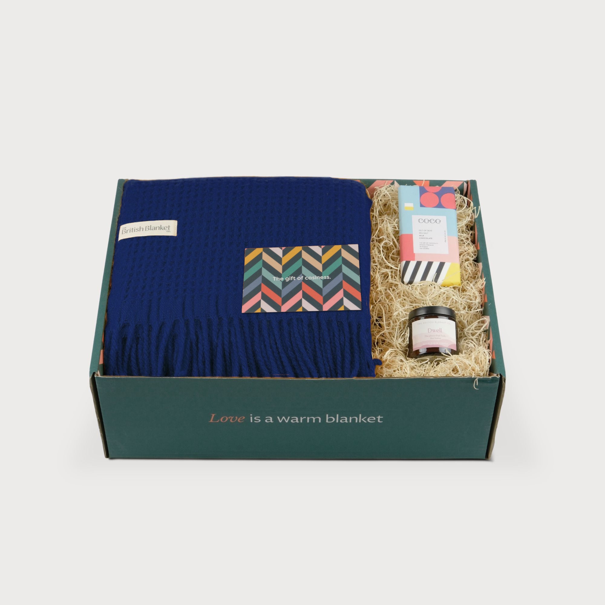 Totterdown Blanket Gift Box: Curious features a navy waffle-weave blanket, a colorful card, a wrapped chocolate bar, and a Dwell jar, all elegantly packaged.