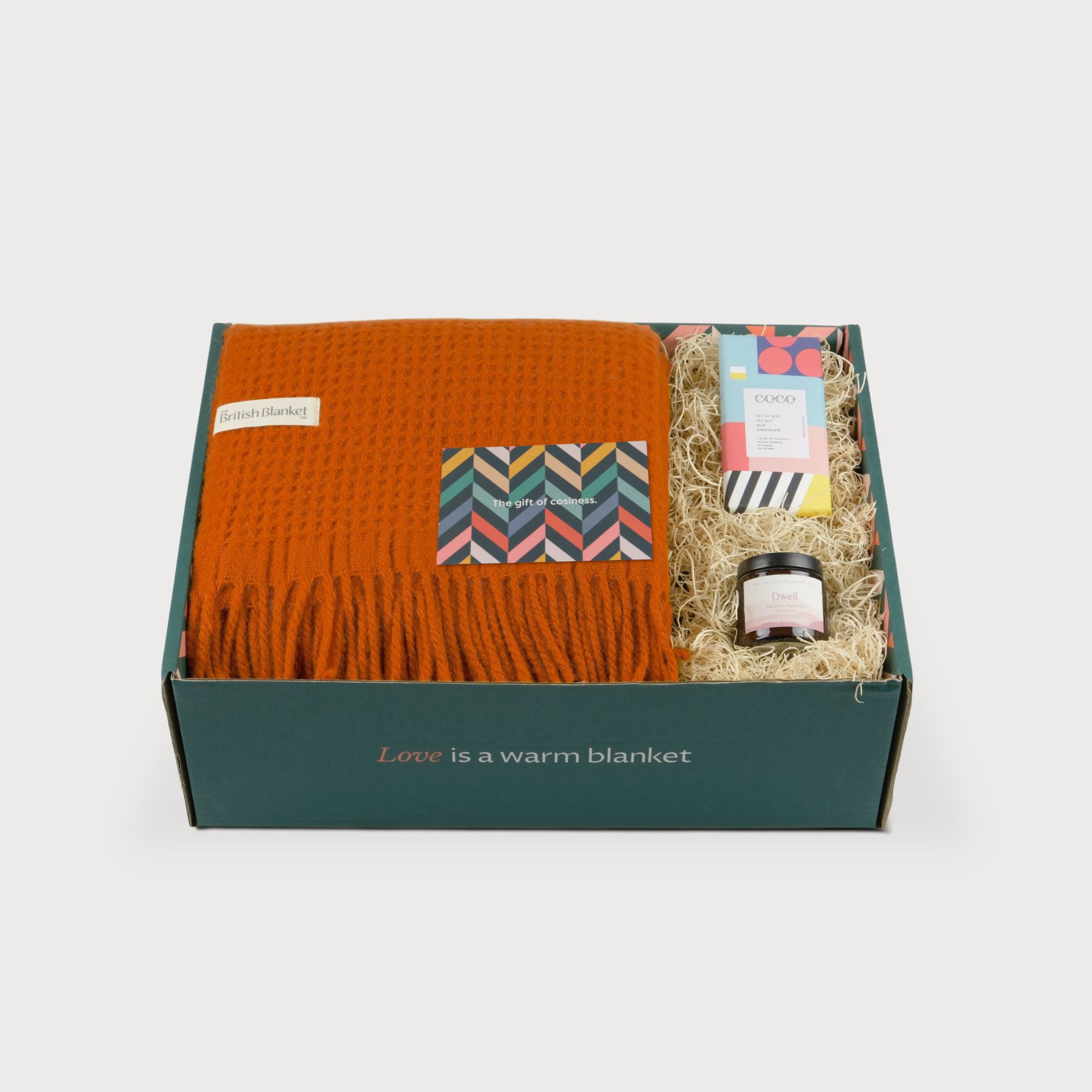 Totterdown Blanket Gift Box: Beacon features a burnt-orange wool blanket, greeting card, artisan chocolate, and amber jar candle, all nestled in a straw-packed box.