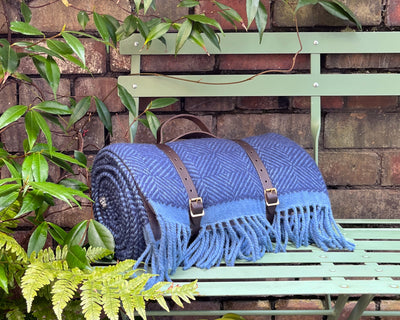 Blue wool picnic blanket with leather straps on bench from The British Blanket Company
