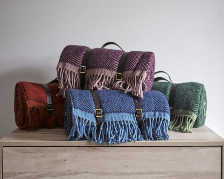 Pile of wool picnic blanket with leather straps on drawers from The British Blanket Company