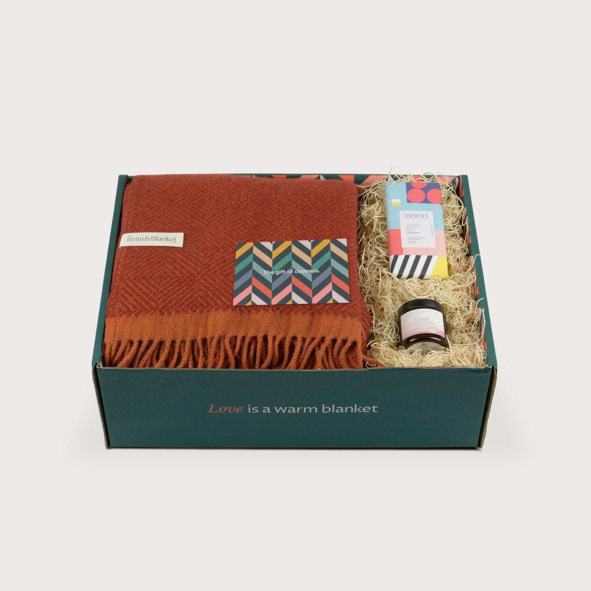 Wildweave Blanket Gift Box: Rowan & Beech, featuring a rust-orange wool blanket, COCO chocolate bar, and amber jar candle in a gift box.