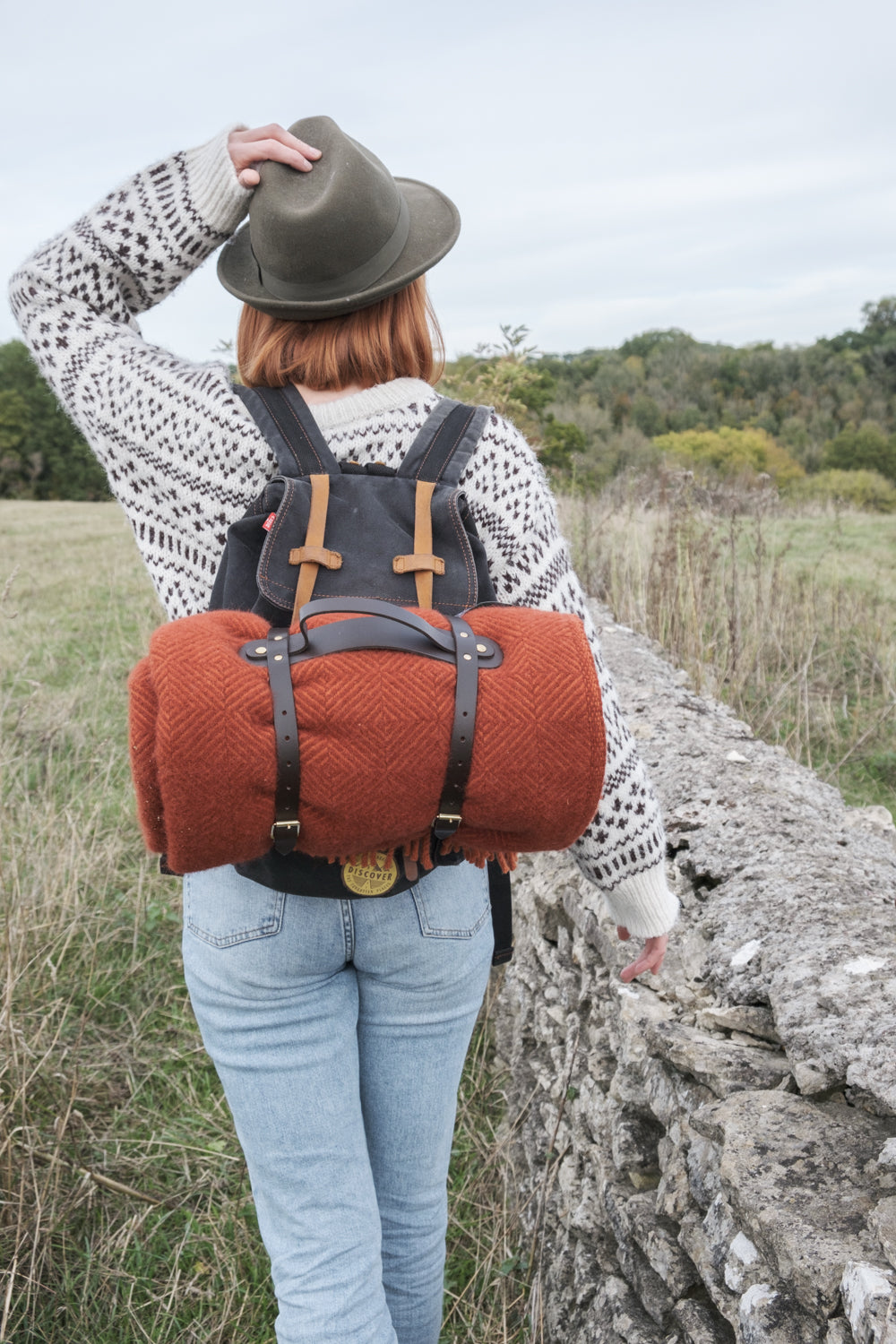 Woman with red wool picnic blanket on backpack rucksack walking through the countryside 