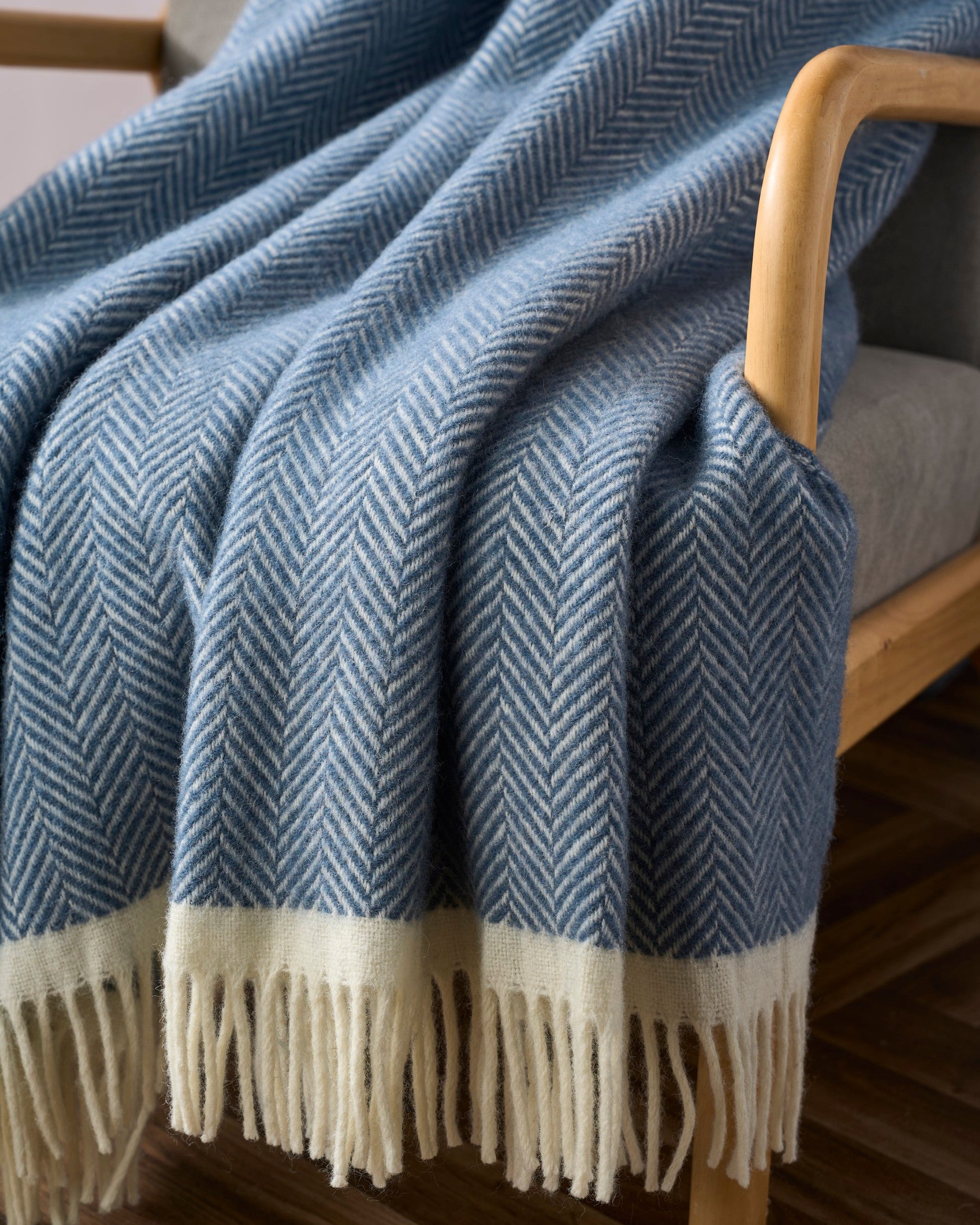 Clifton Blanket Hamper: Steamship, featuring a soft, woven throw with a herringbone pattern, draped over a wooden chair, showcasing a cream fringe.
