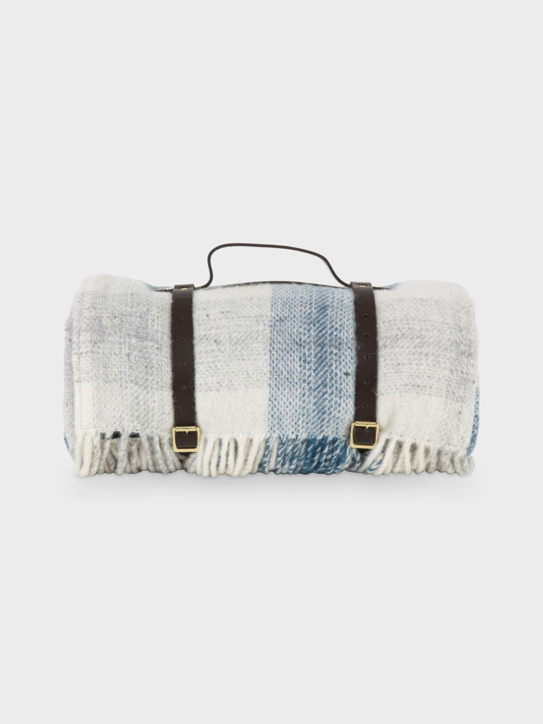 A blue and white wool picnic rug by The British Blanket Company. The picnic rug is rolled up with leather straps and a handle.