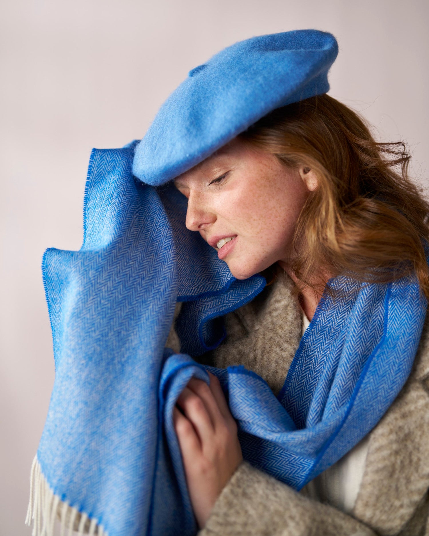 Young woman wearing a Wool Beret Hat: Petrol Blue, showcasing its thicker felt and classic shape, paired with a matching herringbone-patterned scarf.