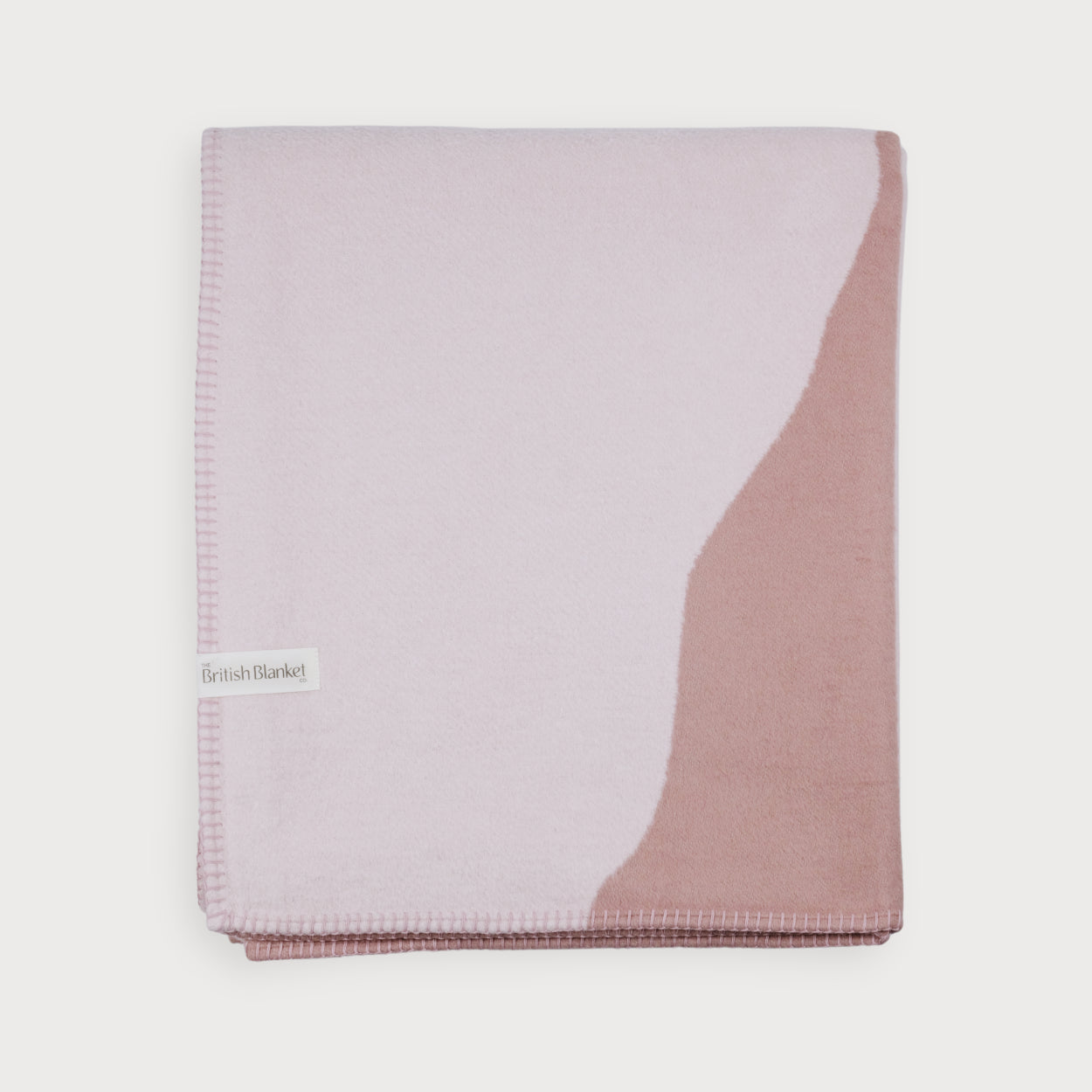 Cloud Cotton Blanket: Vale in Blush, folded neatly, showcasing soft, muted pink tones, whip-stitched edge, and a “British Blanket Co.” label, exuding contemporary style.
