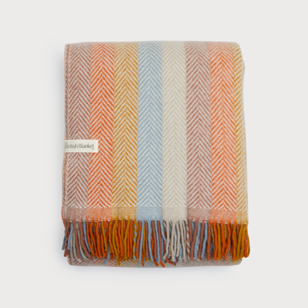 Rainbow Stripe Blanket: Boho (C) - A folded wool throw with pastel herringbone stripes, fringed edges, and a woven label from The British Blanket Co.