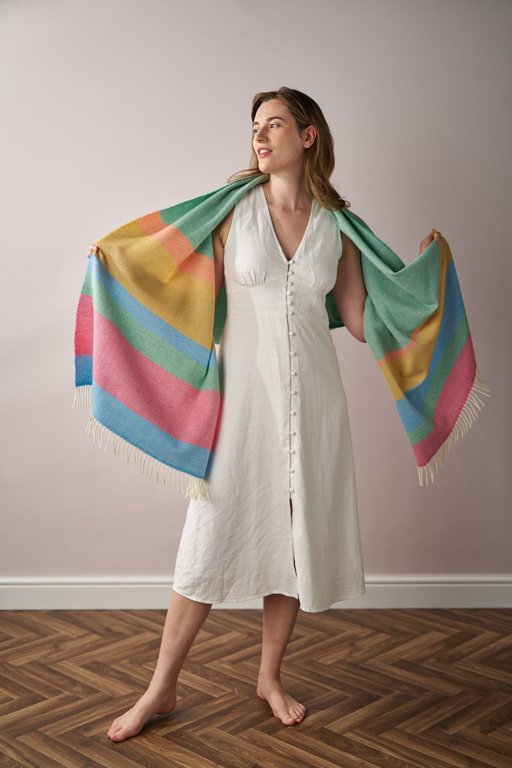 Woman in white dress holding the Oversized Blanket Scarf in Sorbet Stripe over her shoulder indoors.