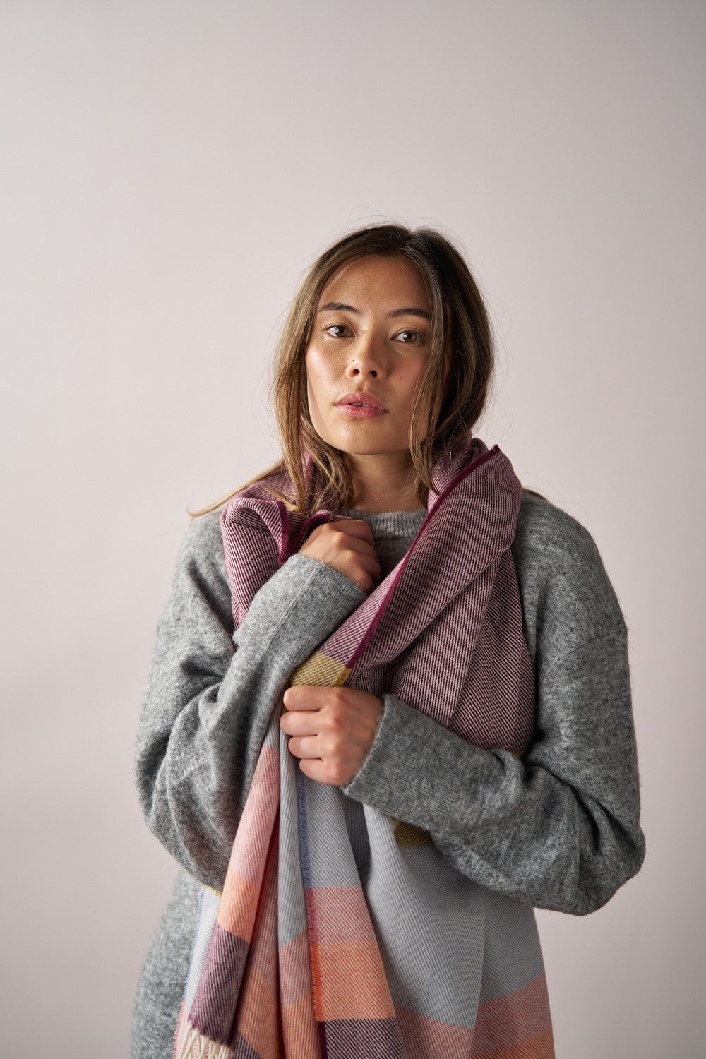 Woman holding the Oversized Blanket Scarf: Berry Stripe, crafted from merino lambswool, showcasing its warm, luxurious texture.