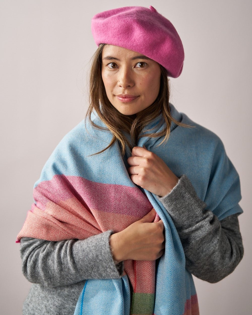 Oversized Blanket Scarf: Azure Stripe - A woman wearing a pink beret, blue sweater, and multi-colored scarf.