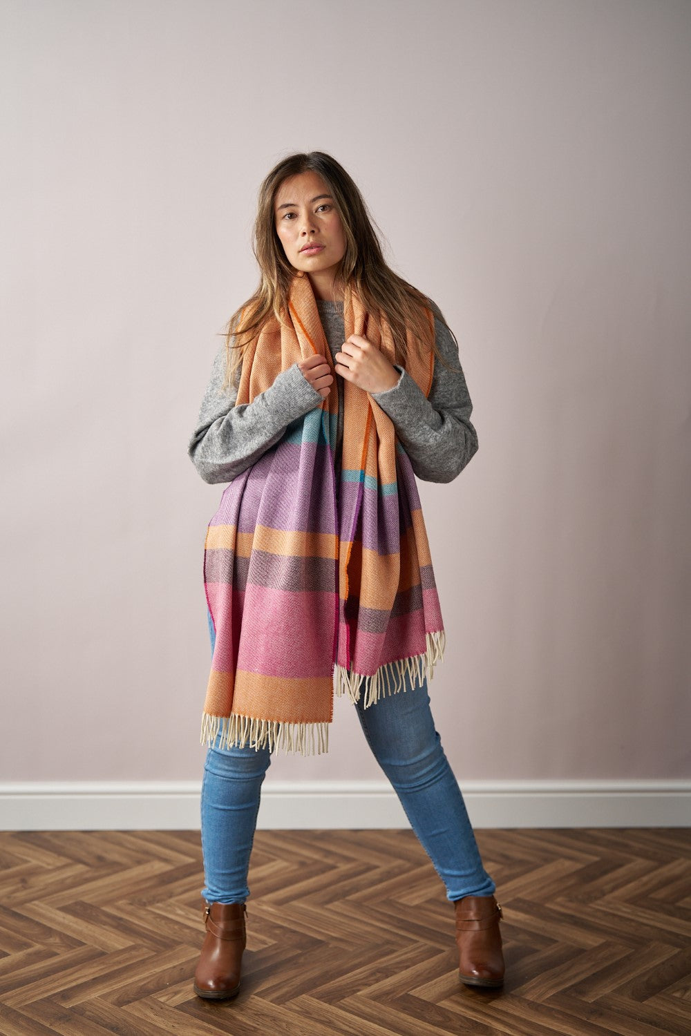 Woman wearing the Oversized Blanket Scarf: Dahlia Stripe, featuring a fine herringbone weave, styled over casual attire including jeans and boots.