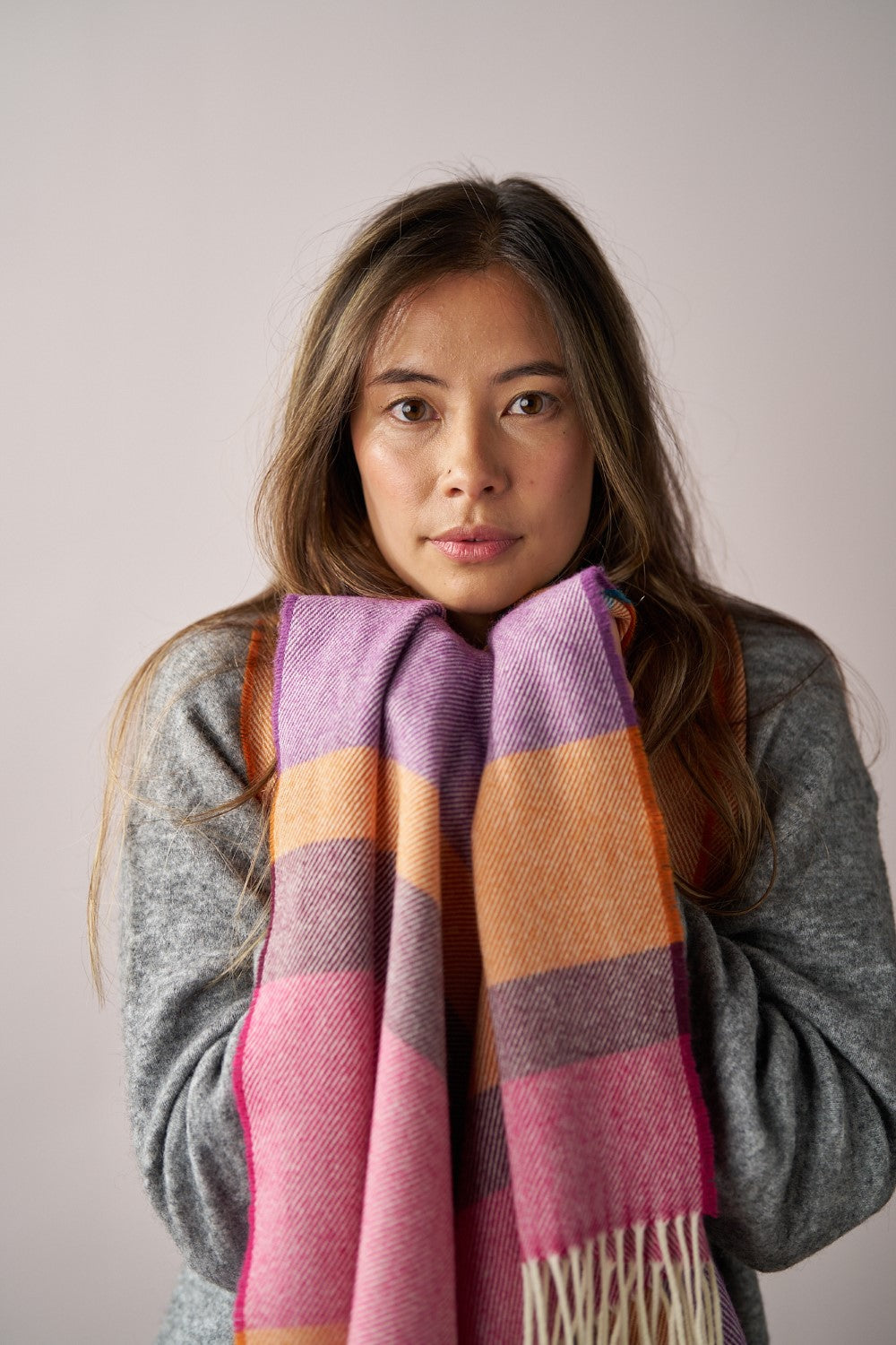 Woman wearing the Oversized Blanket Scarf: Dahlia Stripe, featuring a fine herringbone weave and eye-catching stripes, wrapped around her neck.
