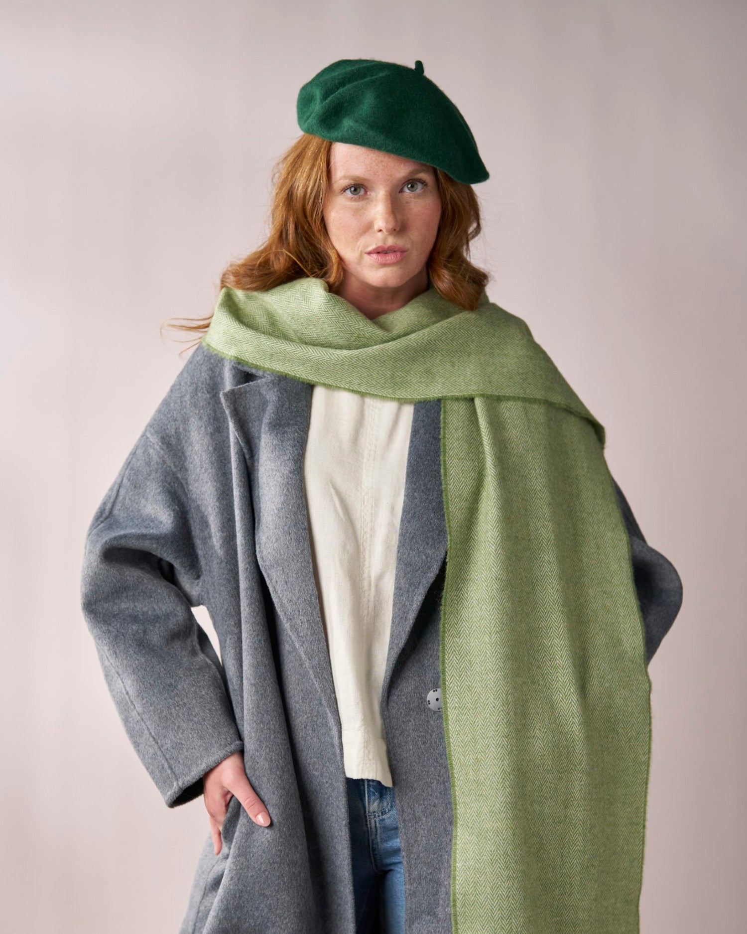 Wool Beret Hat: Dark Green on a woman with reddish hair and freckles, styled with a herringbone scarf, gray overcoat, and jeans, exuding a modern-vintage look.