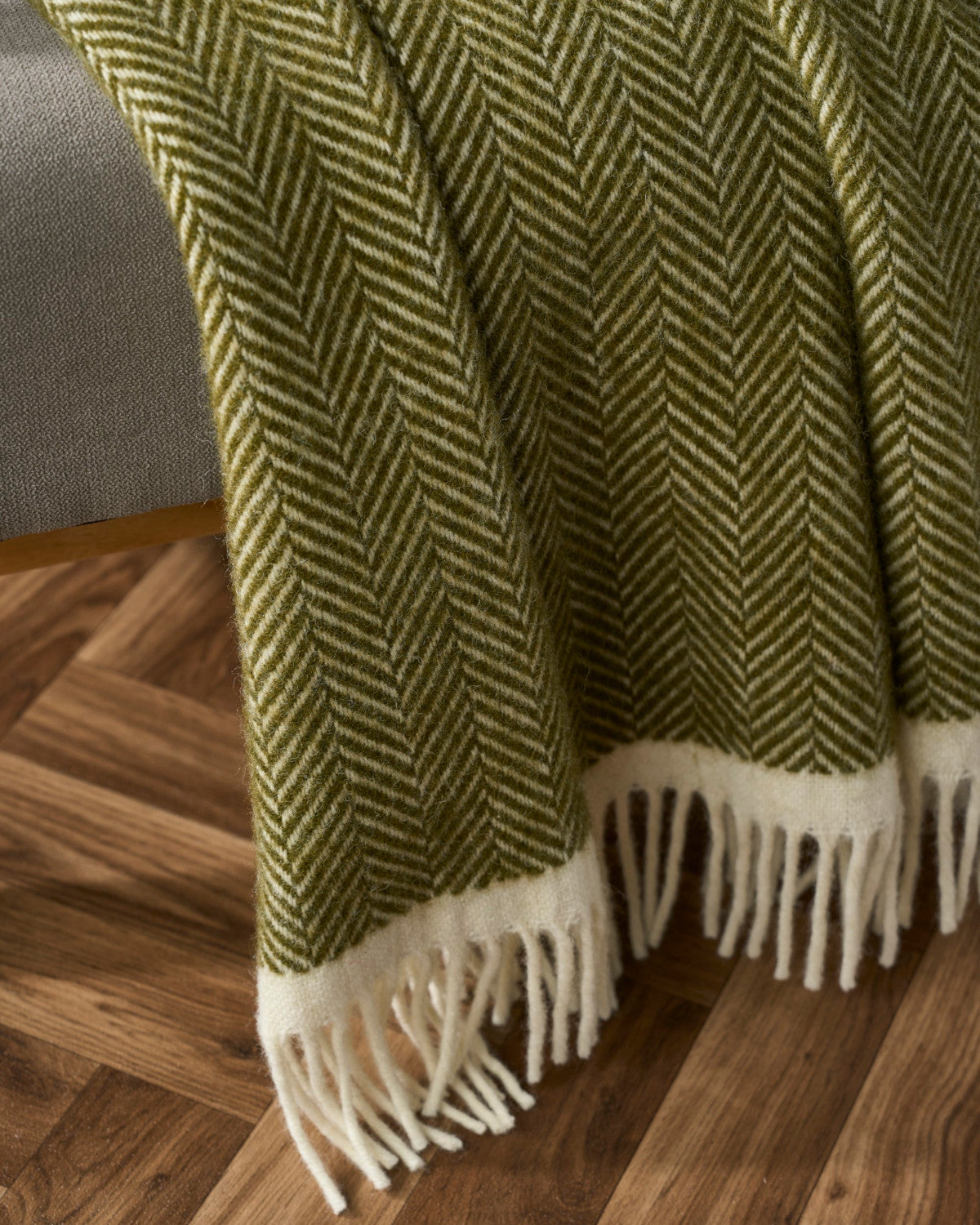 The Christmas Blanket Gift Box: Blaise features a green-and-off-white herringbone throw with a wide off-white band and fringed tassels, draped over a chair.