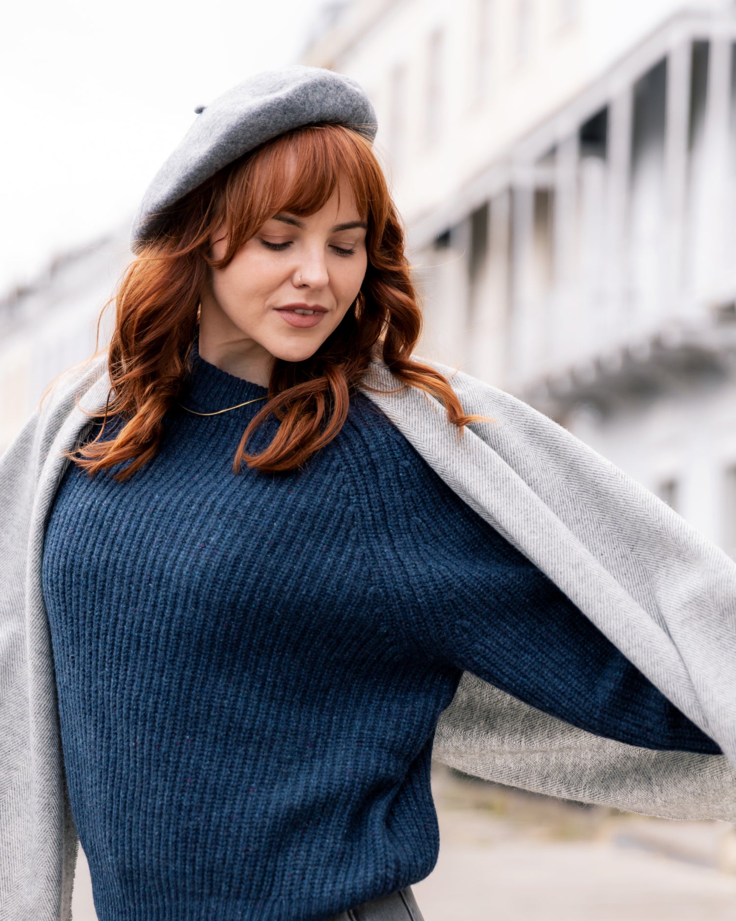 Young woman outdoors wearing a Grey Wool Beret Hat, showcasing its classic style and form, paired with a navy knit sweater and light-gray wrap.