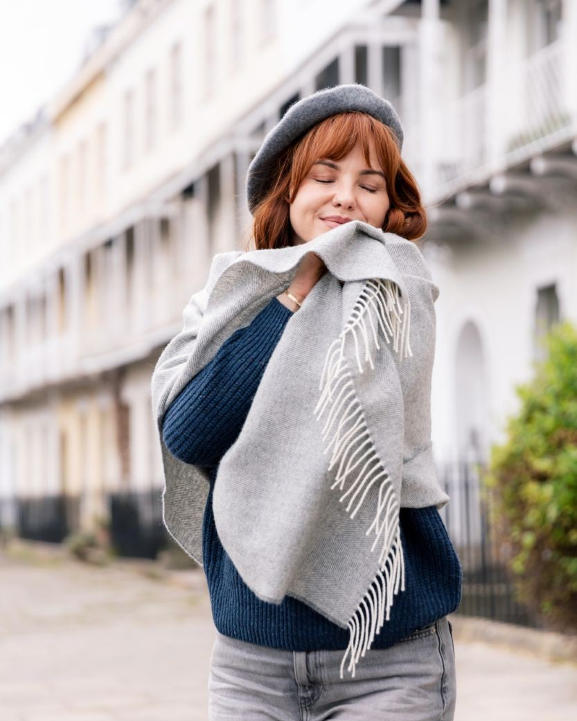 Young woman outdoors wearing a Wool Beret Hat: Grey, showcasing its classic style and warmth, paired with a navy sweater and light-gray shawl.