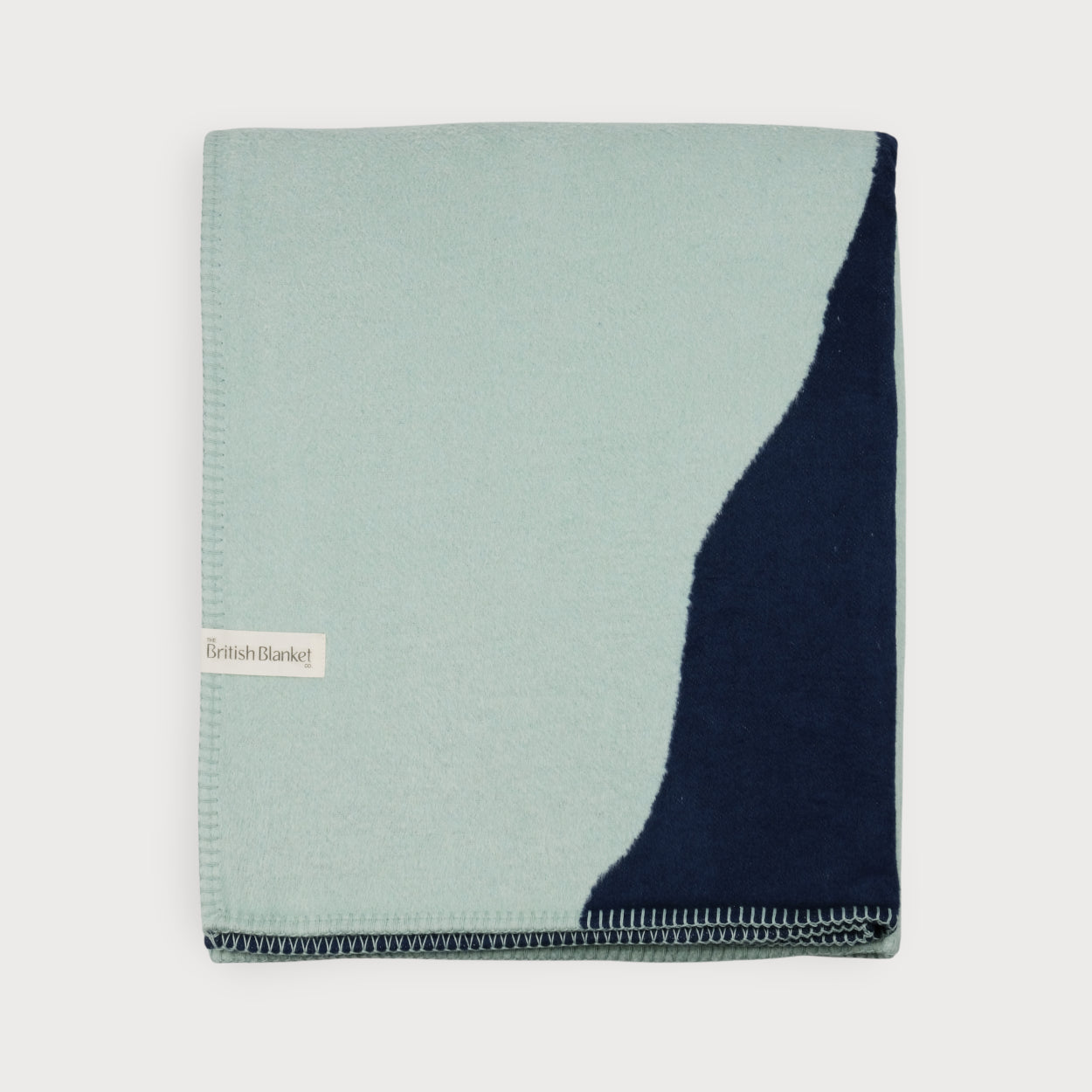 Cloud Cotton Blanket: Vale in Mistral, a two-tone throw featuring pale mint wool and deep navy panel, with “The British Blanket Co.” label, celebrating ten years.