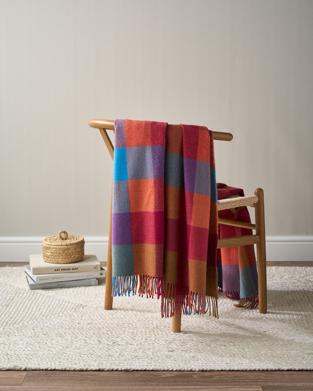 Merino Check Blanket: Multicolour draped over a chair, showcasing its vibrant check pattern and soft texture.