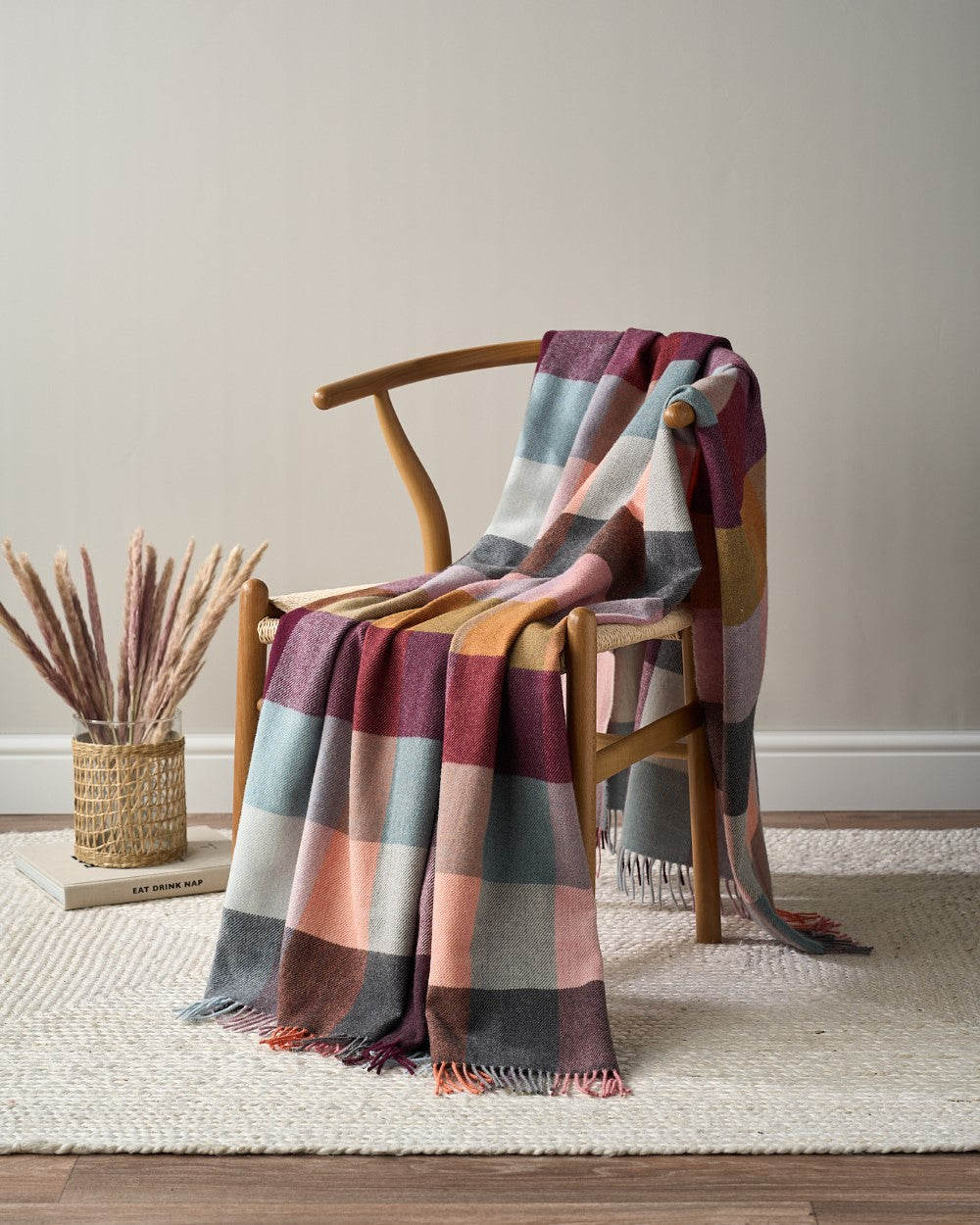Merino Check Blanket: Burnished draped over a chair, showcasing a cozy, autumn-inspired plaid pattern with multicolored tassels.