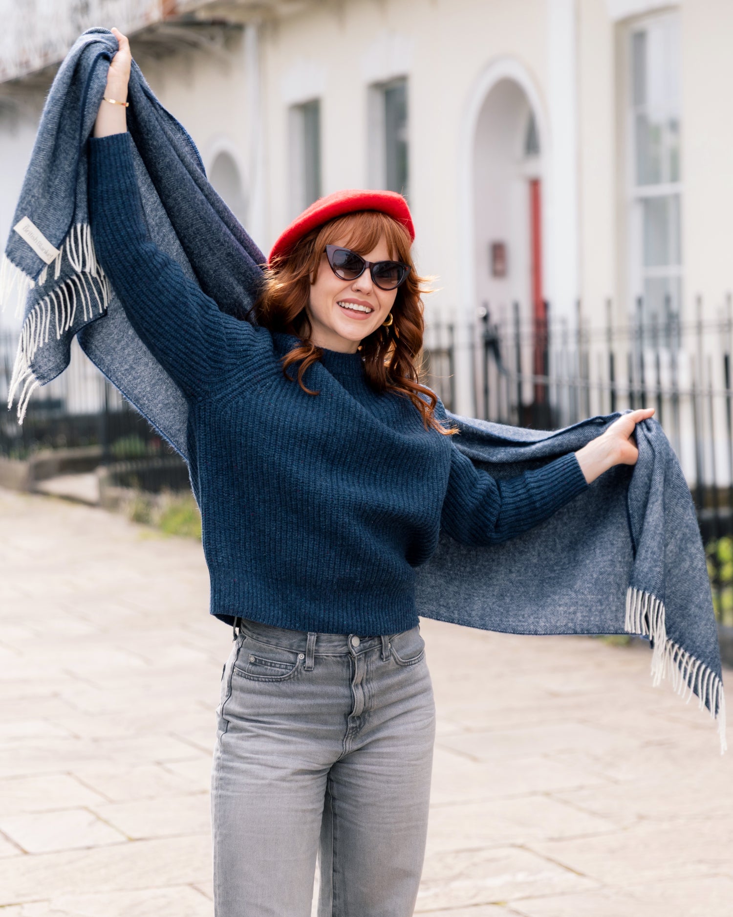 Young woman smiling, wearing an Oversized Blanket Scarf: Navy Blue, draped around her shoulders, showcasing its herringbone texture and ivory tassels.