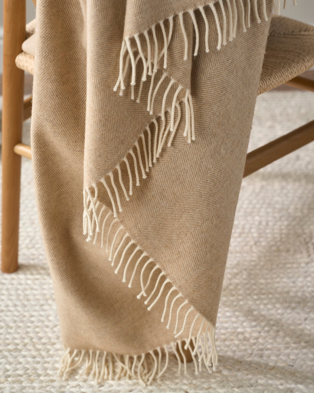 Merino Blanket Gift Box: Basswood, featuring a camel-beige herringbone throw with cream fringe, draped over a wooden chair, perfect for gifting on special occasions.