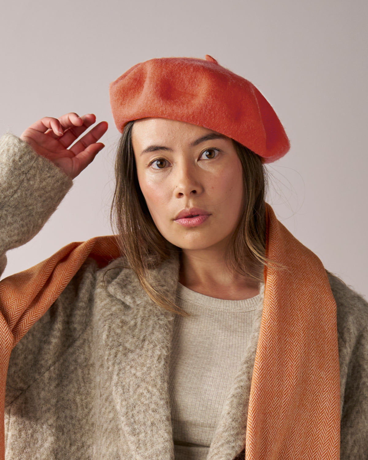 A person wearing a stylish Orange Wool Beret Hat, crafted from premium thick felt, showcasing its vibrant color and quality, paired with a matching scarf.