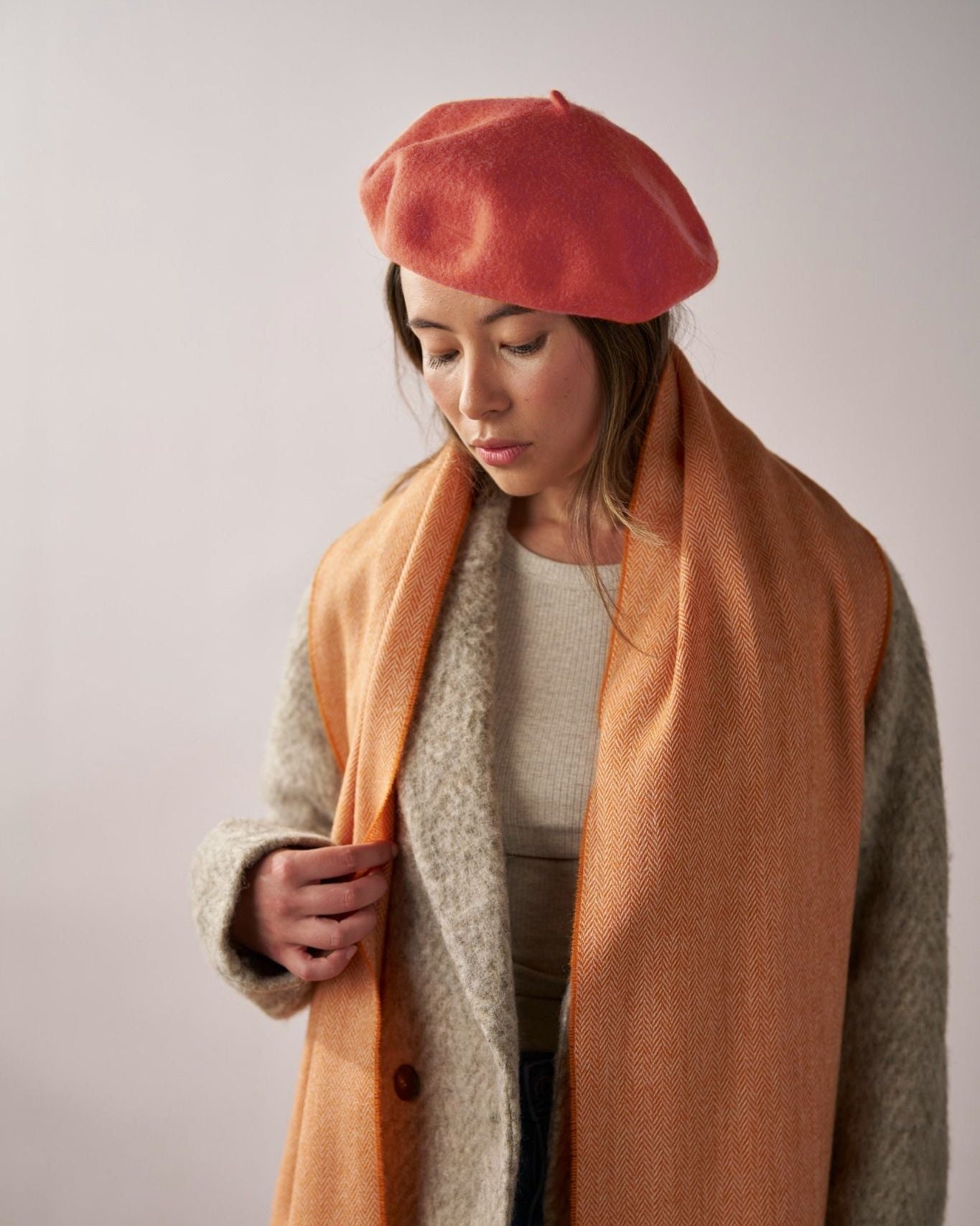Young woman wearing a coral-red Wool Beret Hat: Orange, highlighting its premium thick felt and stylish shape, paired with an orange herringbone scarf.
