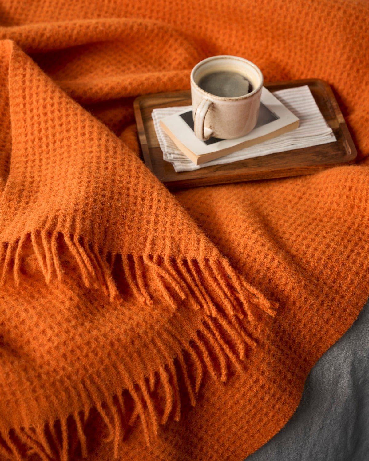 Bright Friday Blanket Bundle: Beacon features an orange waffle-knit throw with fringed edges, draped with a wooden tray holding a book and coffee mug.