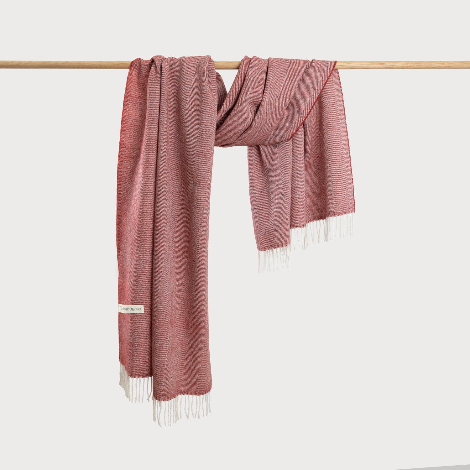 Oversized Blanket Scarf Gift Box: Tabasco, featuring a woollen throw with a herringbone pattern, white fringe, and a British Blanket label, draped over a wooden rod.