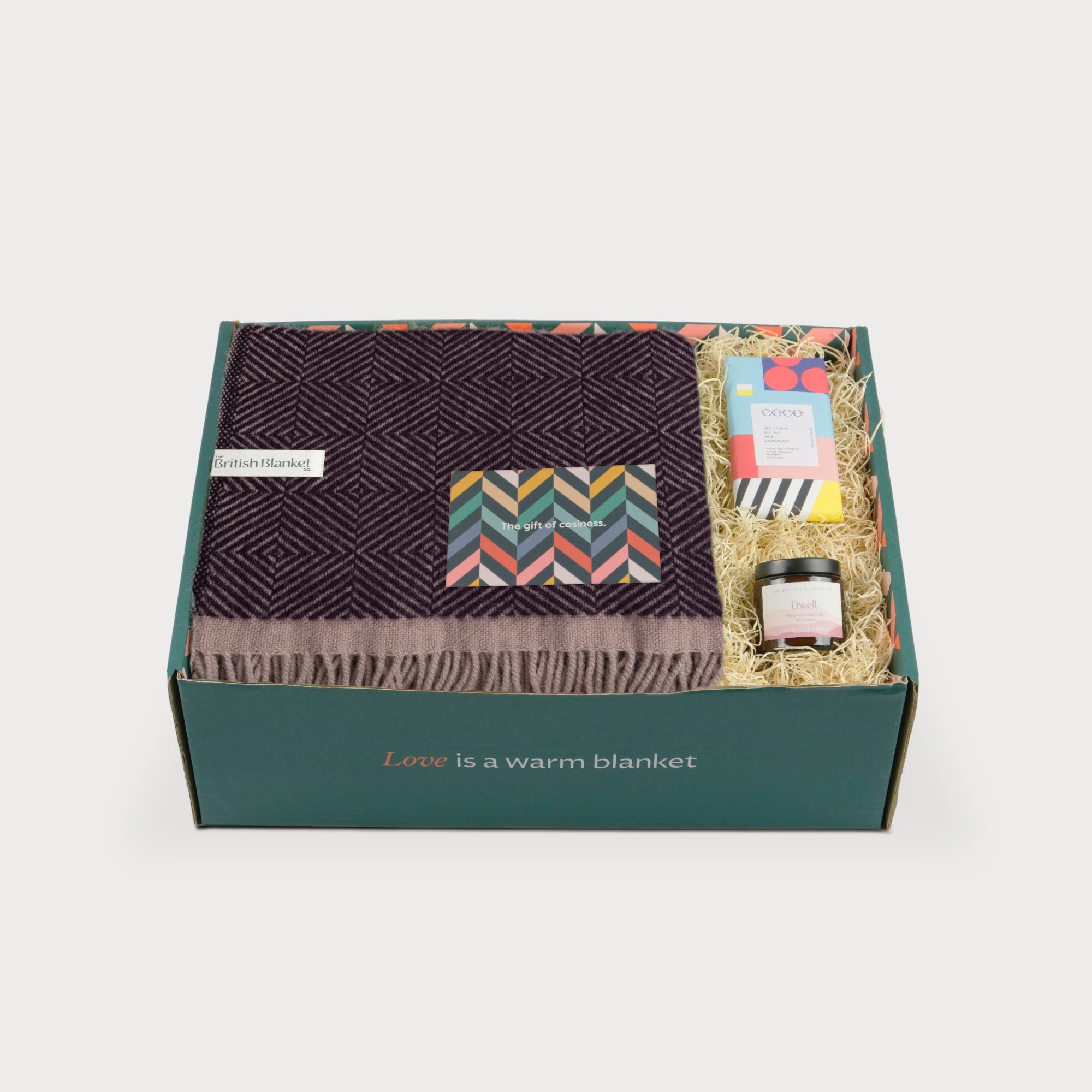 Wildweave Blanket Gift Box: Blackberry & Heather includes a purple-patterned wool blanket, greeting card, COCO chocolate, and Dwell candle in a green gift box.