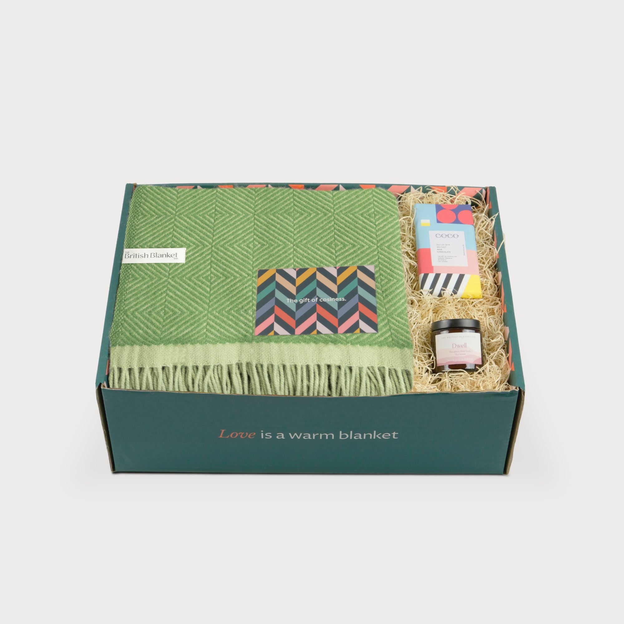 Wildweave Blanket Gift Box: Fennel & Catkin featuring a green wool blanket, patterned chocolate bar, and Dwell spread, elegantly arranged in a printed box.