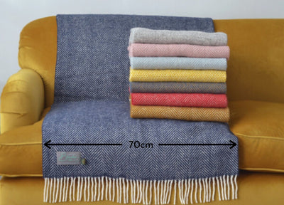 Folded wool blankets stacked on a yellow sofa. A blue wool throw measuring 70 centimeters in width is draped over the sofa