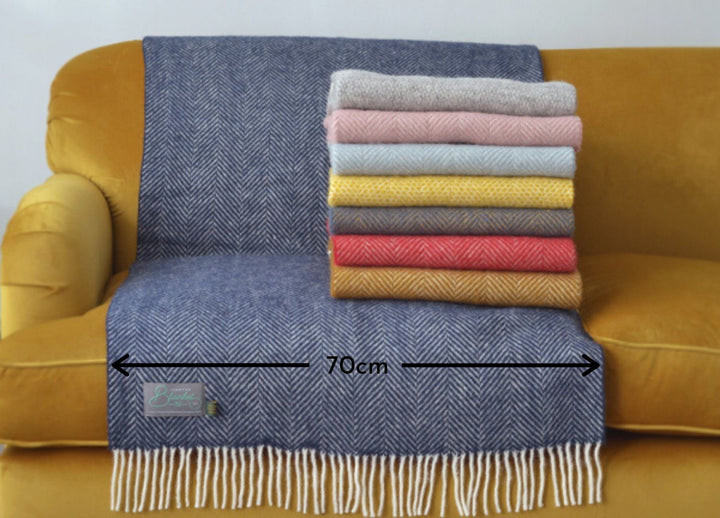 A stack of folded wool throws on a yellow sofa. A blue blanket measuring 70 centimeters is draped over the sofa