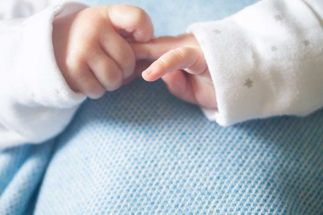 A baby's hands on top of a blue lambswool baby blanket