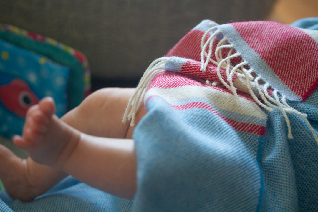 A baby's feet poking out of a red and blue lambswool baby blanket