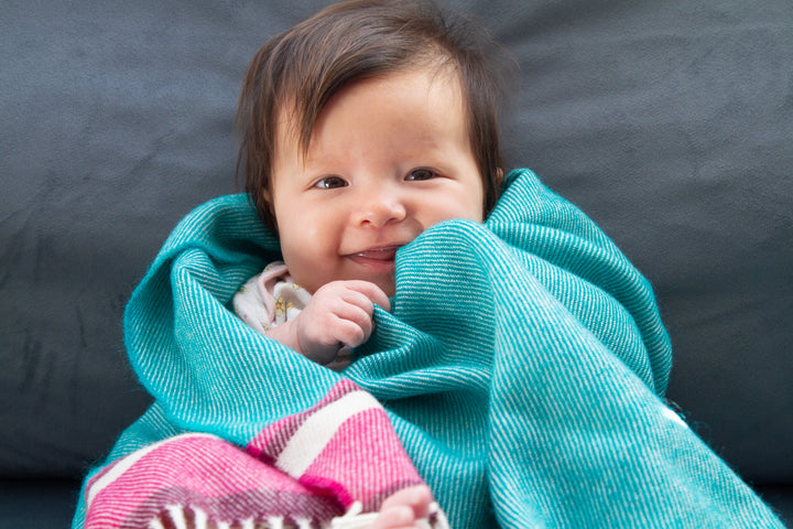 A baby wrapped in a blue merino lambswool baby blanket