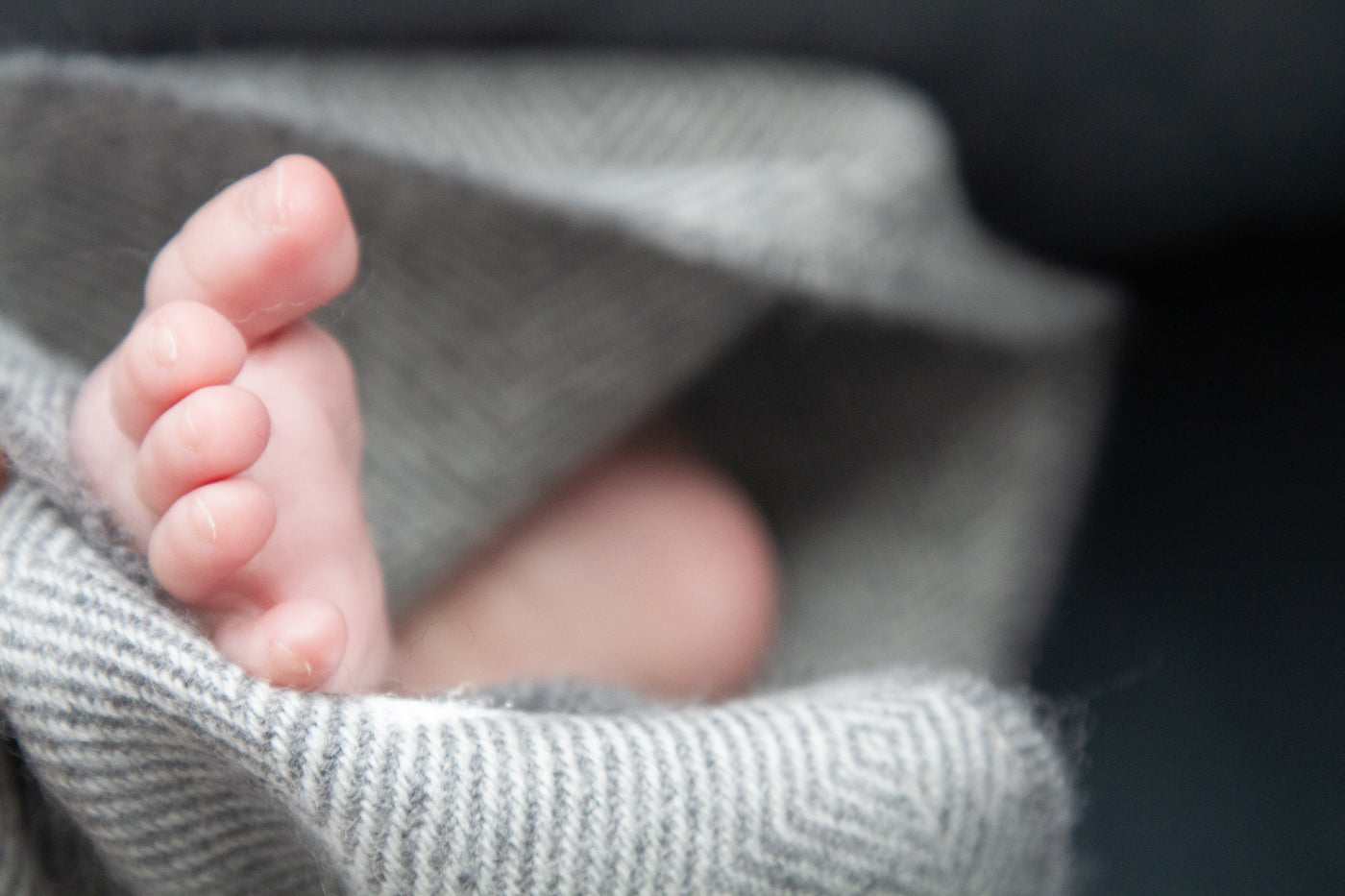 Closeup of a baby's foot peaking out of a grey wool baby blanket. 