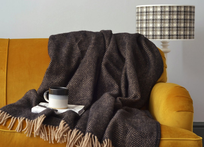 A black herringbone wool blanket draped on a yellow sofa. 
