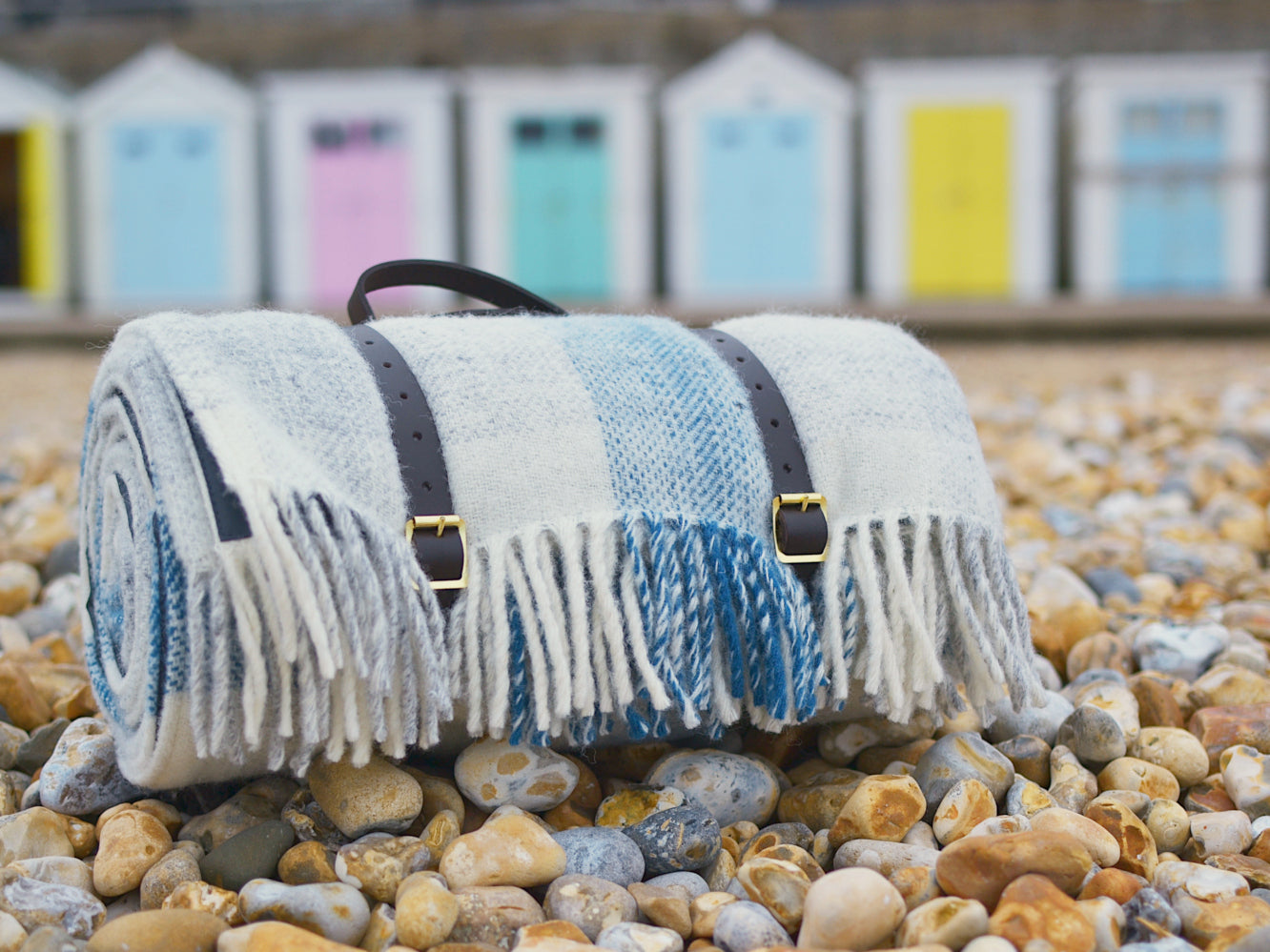 Closeup of a blue and white picnic rug on a stone beach. The picnic rug is rolled up with leather straps. 